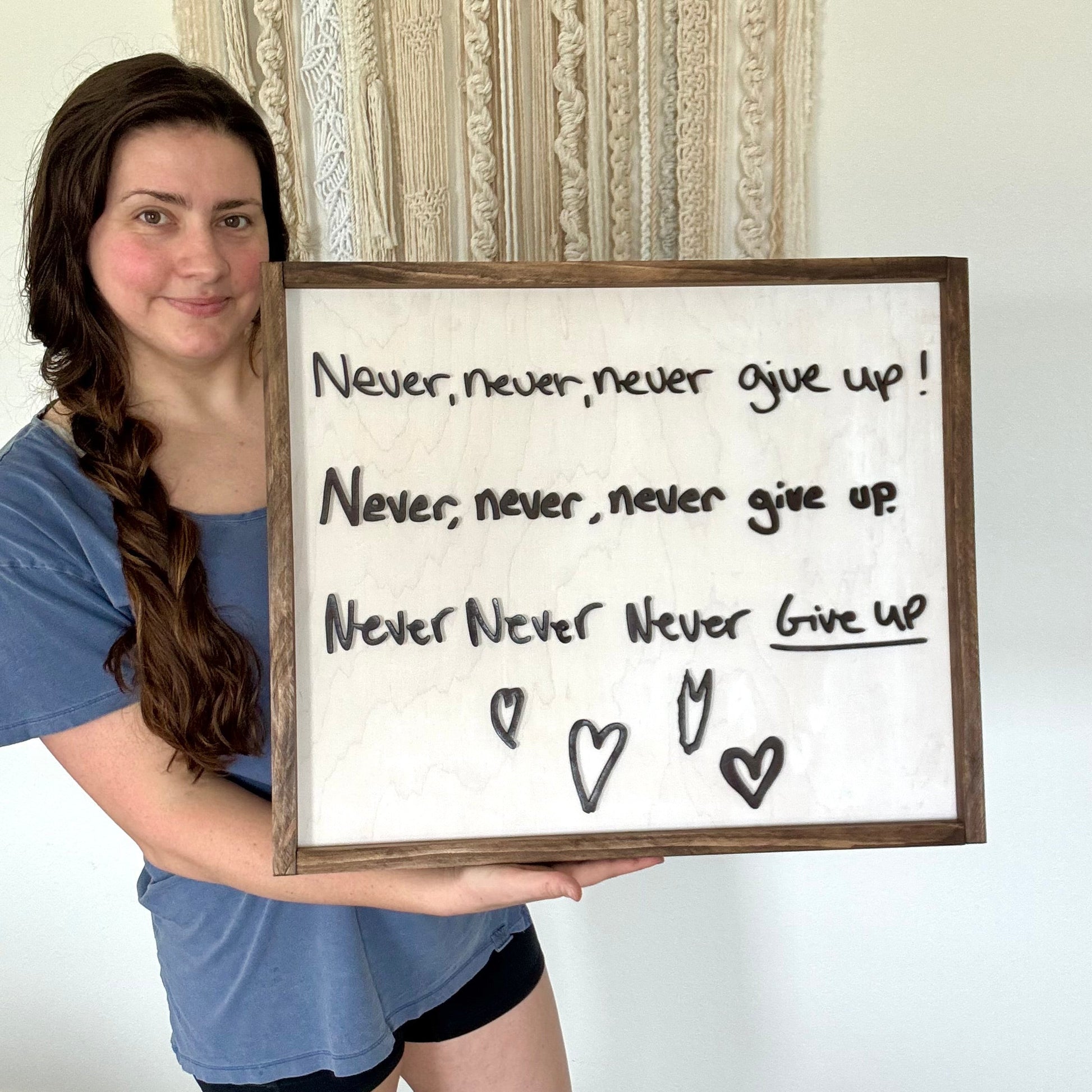 Person holding a framed motivational quote with hearts on a plain background