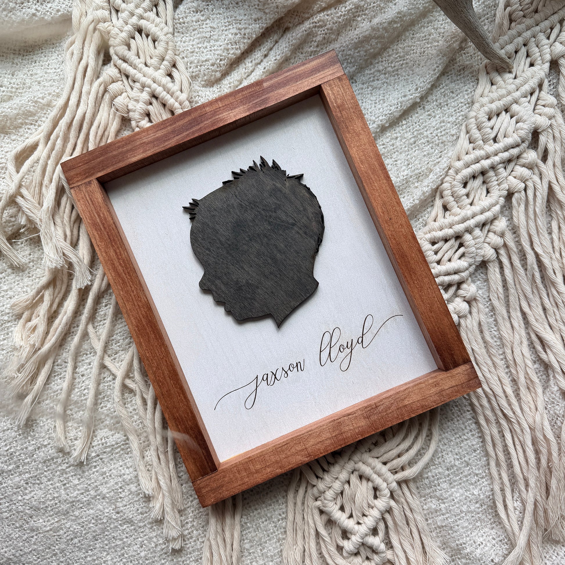 Framed leaf with 'Jaxson Lloyd' text on a textured surface with macrame and antlers.